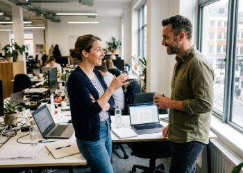 Two colleagues having a candid one-on-one conversation at a desk in a bright office