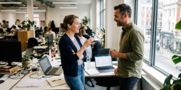 Two colleagues having a candid one-on-one conversation at a desk in a bright office