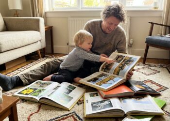Parent and young child reading colorful nonfiction fact books together on a rug